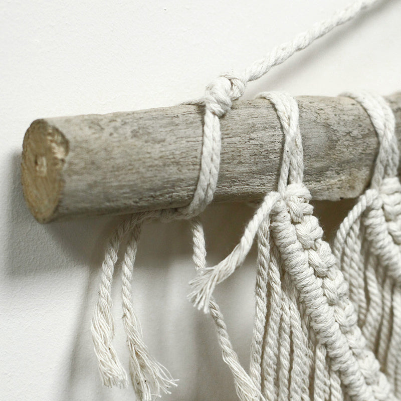 Macrame wall hanging with a wooden stick on a white background