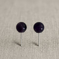 Pair of black spherical earrings on a beige fabric background