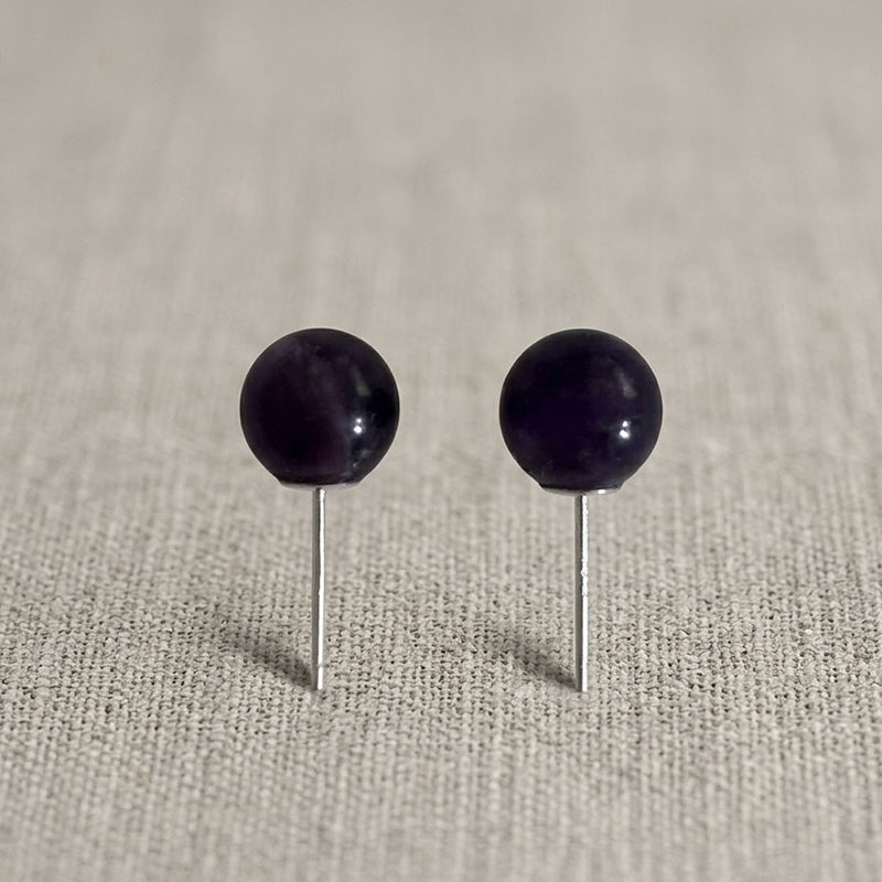 Pair of black spherical earrings on a beige fabric background