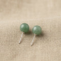 Pair of green round earrings on a beige fabric background