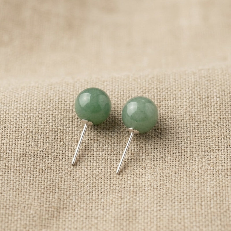 Pair of green round earrings on a beige fabric background