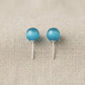 Pair of turquoise ball earrings on a beige fabric background