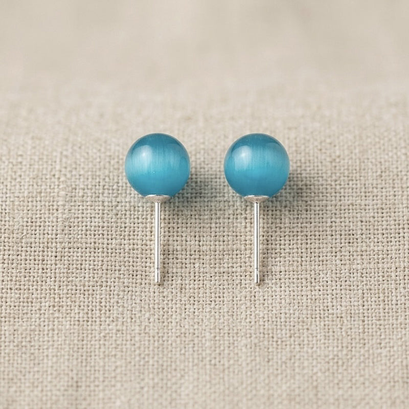 Pair of turquoise ball earrings on a beige fabric background