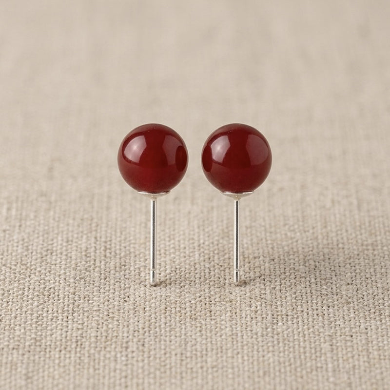 Pair of red spherical earrings on a beige fabric background