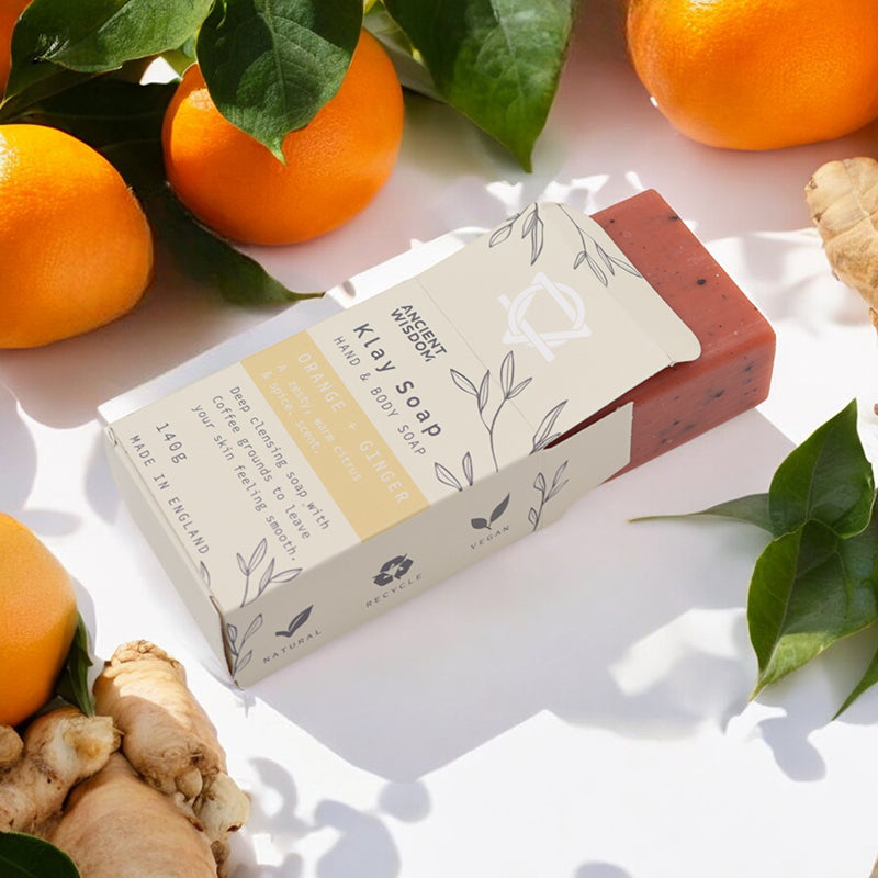 Klay Soap bar with packaging on a white surface surrounded by oranges and ginger.