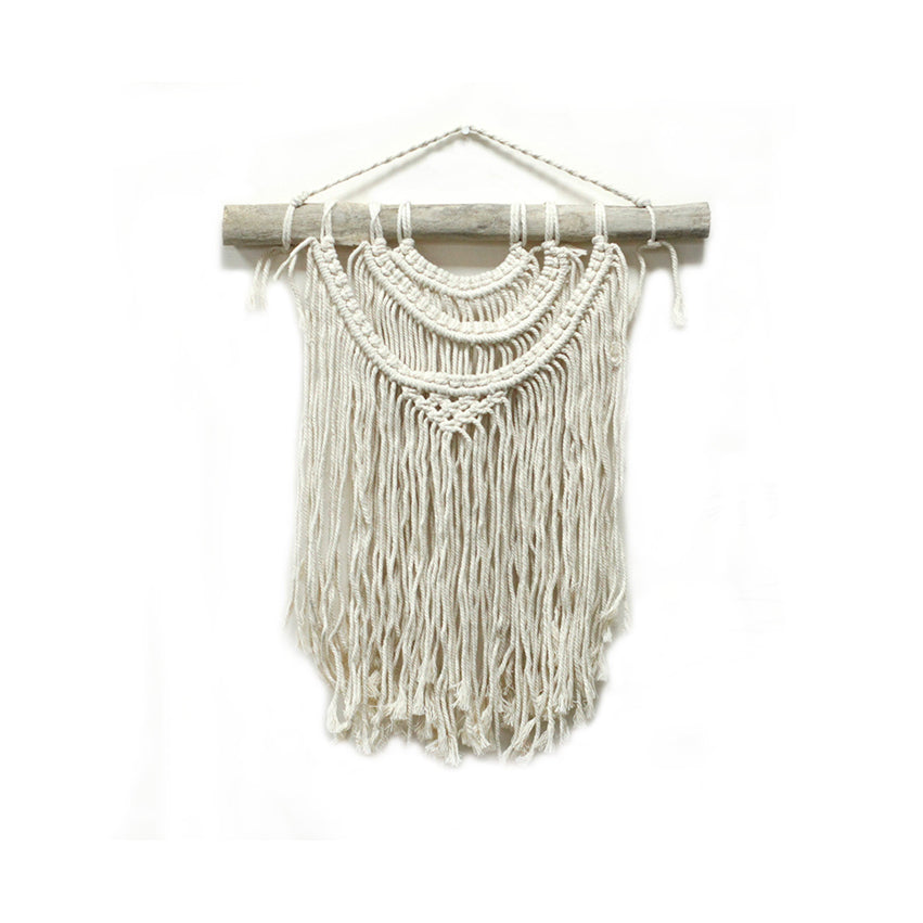 Macrame wall hanging with white strings on a wooden stick against a white background